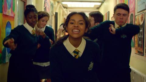 A group of school children singing in a school corridor.