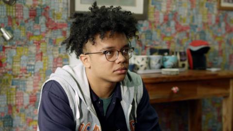 A boy with glasses sits with a sad expression.