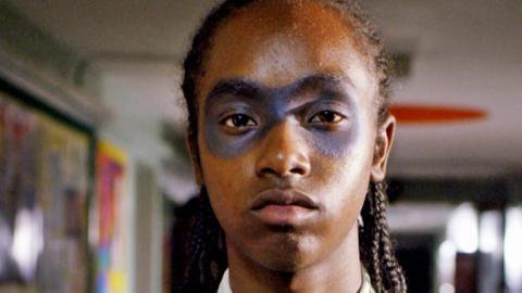 A boy with eye makeup on looking serious.