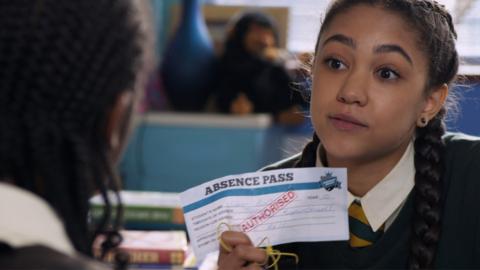 A girl holding up a piece of paper saying 'Absence Authorised.'