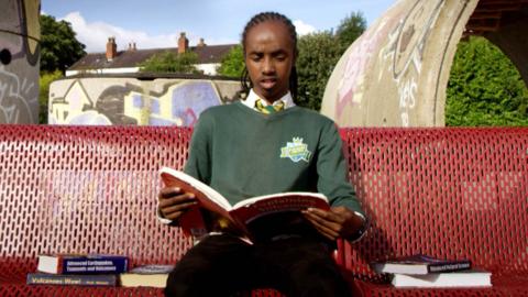 A boy sits on a bench reading a book.