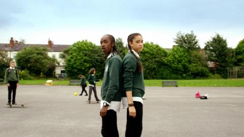 A boy and a girl stand back to back in a playground looking sad.