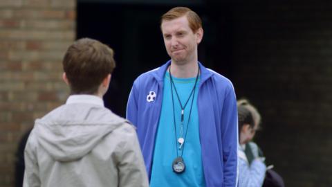 A sports teacher looks unimpressed at a pupil.