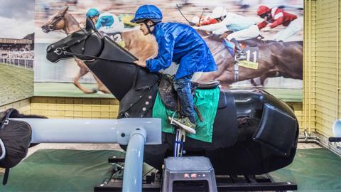 A young visitor dressed as a jockey rides an animatronic racehorse at the Palace House.