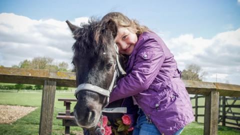 girl-in-purple-coat-hugging-a-pony.