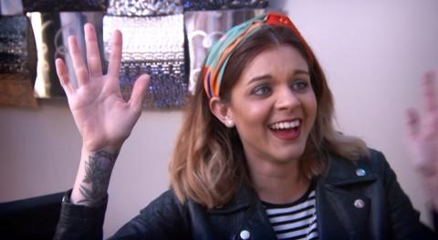 A woman waves her hands in the air, grinning.