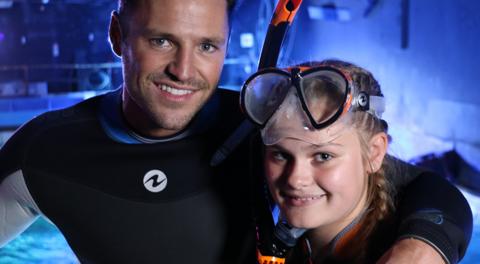 A man and a girl wearing snorkles pose in front of a shark tank.