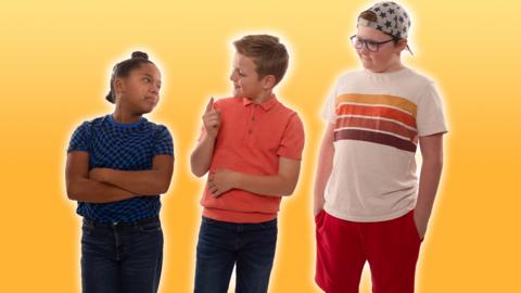 From left to right: a small, black girl with her arms folded looking at a small white boy pointing his finger up and a slightly taller, small, plus sized boy with glasses and a backwards cap looking at them both.