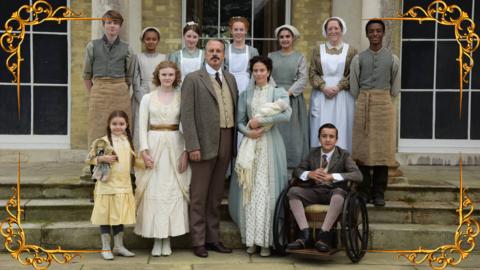 A formal Victorian family photo, with the family of the house stood in front, smiling, with the serving staff stood behind them on the steps of the stately house, set in a gold frame.