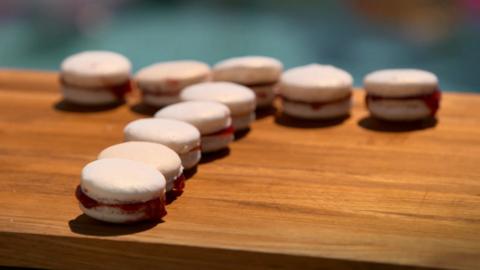 Ten macarons arranged into a 'T' shape with raspberry jam sit on a wooden board.