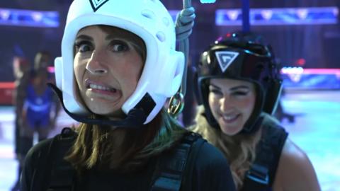 Alex Jones from Morning Live wearing a white helmet looks nervous, Sabre from Gladiators is behind her grinning.