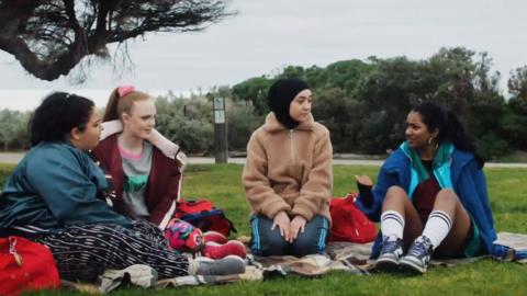 A group of girls from Mustangs FC have a picnic in a park.