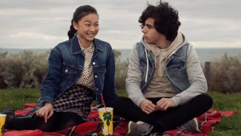 A boy and a girl from Mustangs FC sit on a hill close together.