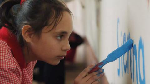 A girl paints on a wall with a large paintbrush.