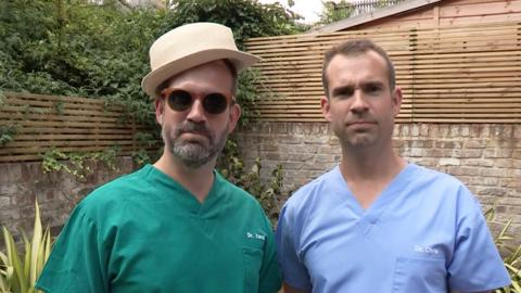 Dr Chris and Dr Xand are standing outside. Dr Xand is wearing sunglasses and a hat.