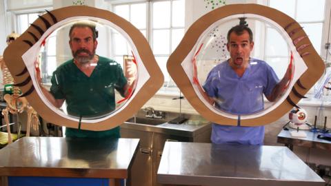 Doctors Chris and Xand pose holding two giant eye models.