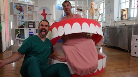 Doctors Chris and Xand pose with a giant model of a mouth.