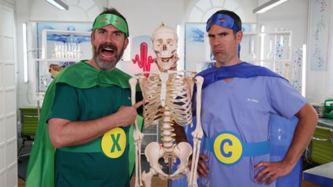 Doctor Chris and Xand wear superhero costumes with their skeleton prop.