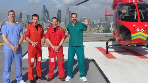 Dr Xand and Dr Chris standing with two medical professionals. They are all pulling faces and are standing on a helipad, on the  top of the roof and next to a helicopter.