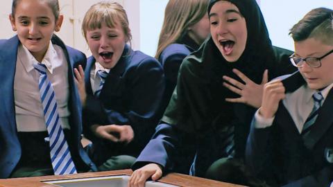 Students stand near a workbench in a science lab looking disgusted and shocked.