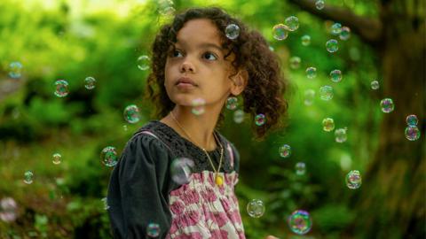 A young girl surrounded by bubbles in a forest