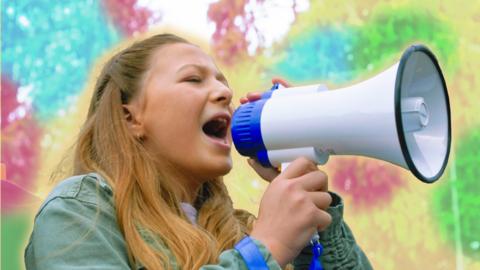 A young blonde girl is shouting into a megaphone