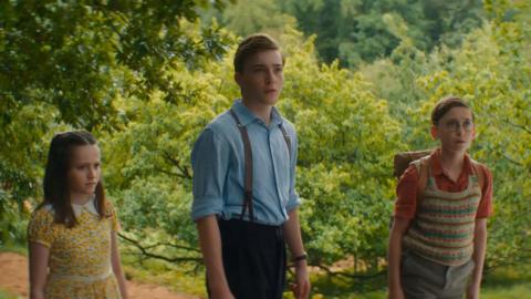 From L to R: a small white girl with long brown hair, a teenage white boy with short blonde hair and a small white boy with glasses and short brown hair are all looking into the distance at something out of frame.