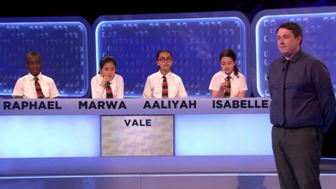 There is a panel of four students and a man stands next to them.