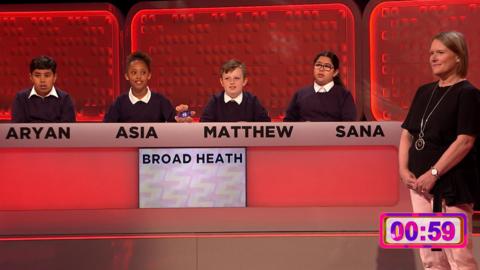 Teacher stands next to pupils who are sitting behind a panel.