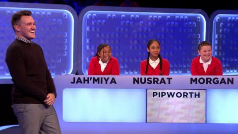 Teacher stands next to three students who are behind a panel.