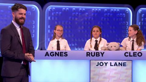 Teacher stands next to his four pupuls who are sitting behind a panel.