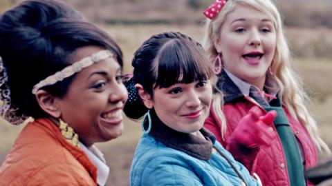 Three girls smiling in brightly coloured coats standing in a row.