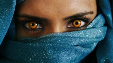 A girl with bright yellow eyes stares with determination with the rest of her face covered by her hijab.