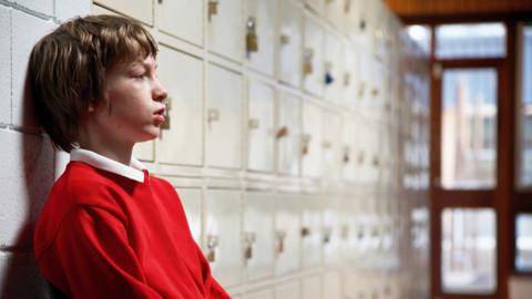 A boy alone at school, looking sad.