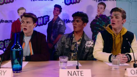 Harry, Nate and Oakley sit behind a desk with shocked faces.