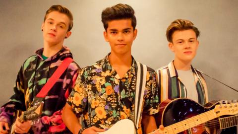 Three boys with guitars stand together in a group, the boys from The Wonderland.