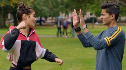 Chloe and Nate are sparring in a park.