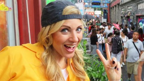 Naomi Wilkinson showing a 'peace' sign with her fingers on an Asian street.