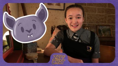 A girl sat at her desk with a bat emoji next to her. Felicity Foxglove from The Worst Witch.