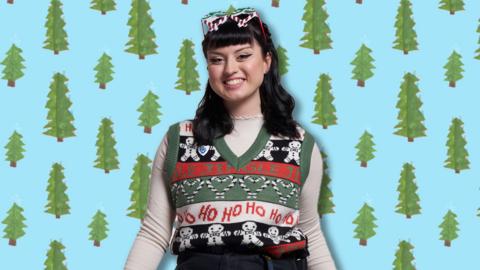 Abby in a Christmas Jumper on a christmas tree patterned background.