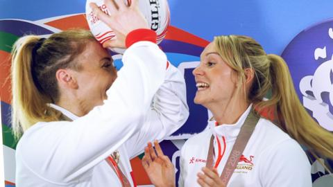 Netballers Jade Clarke and Natalie Haythornthwaite, laughing. Jade is holding a netball above her head.