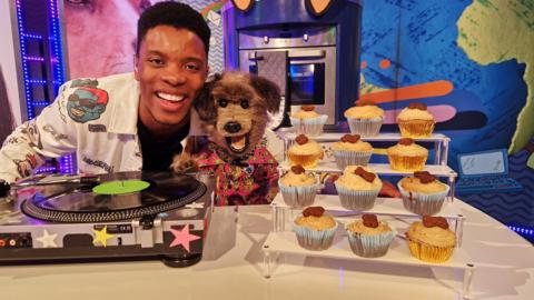 C˿'s Rhys and Hacker the dog smile and show various cupcakes made for dogs, it is made of banana and peanut butter and decorated with a dog treat.