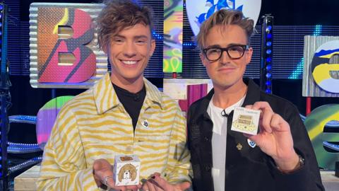 Blue Peter presenter Joel and Tom Fletcher hold up a story cube that they have made.