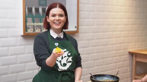 Lindsey is wearing a green Blue Peter apron and is holding out a wonton to the camera.