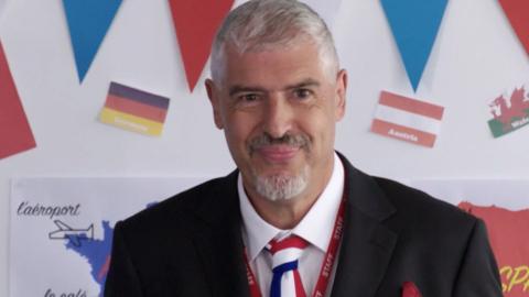 A man smiling, surrounded by French flags.