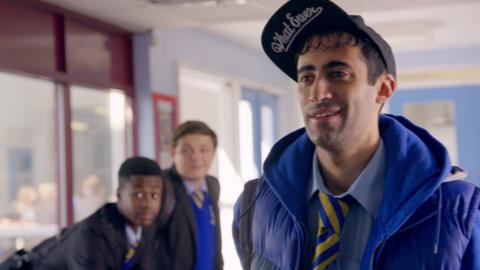 A boy in school smiling with his friends looking at him in the distance.