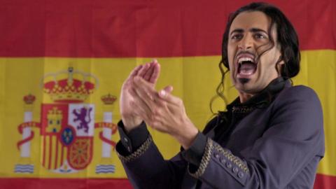 A Spanish flag on the wall with a man shouting in front of it.