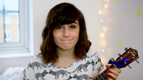 Dodie smiling and playing a ukelele