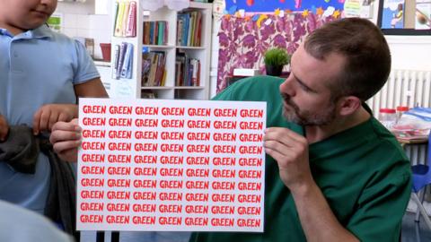 A doctor leans forwards, holding a sign that reads 'Green Green Green' in red.