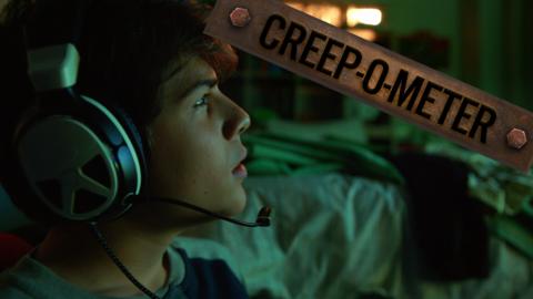 A boy sat in a dark room wearing a headset, playing video games.